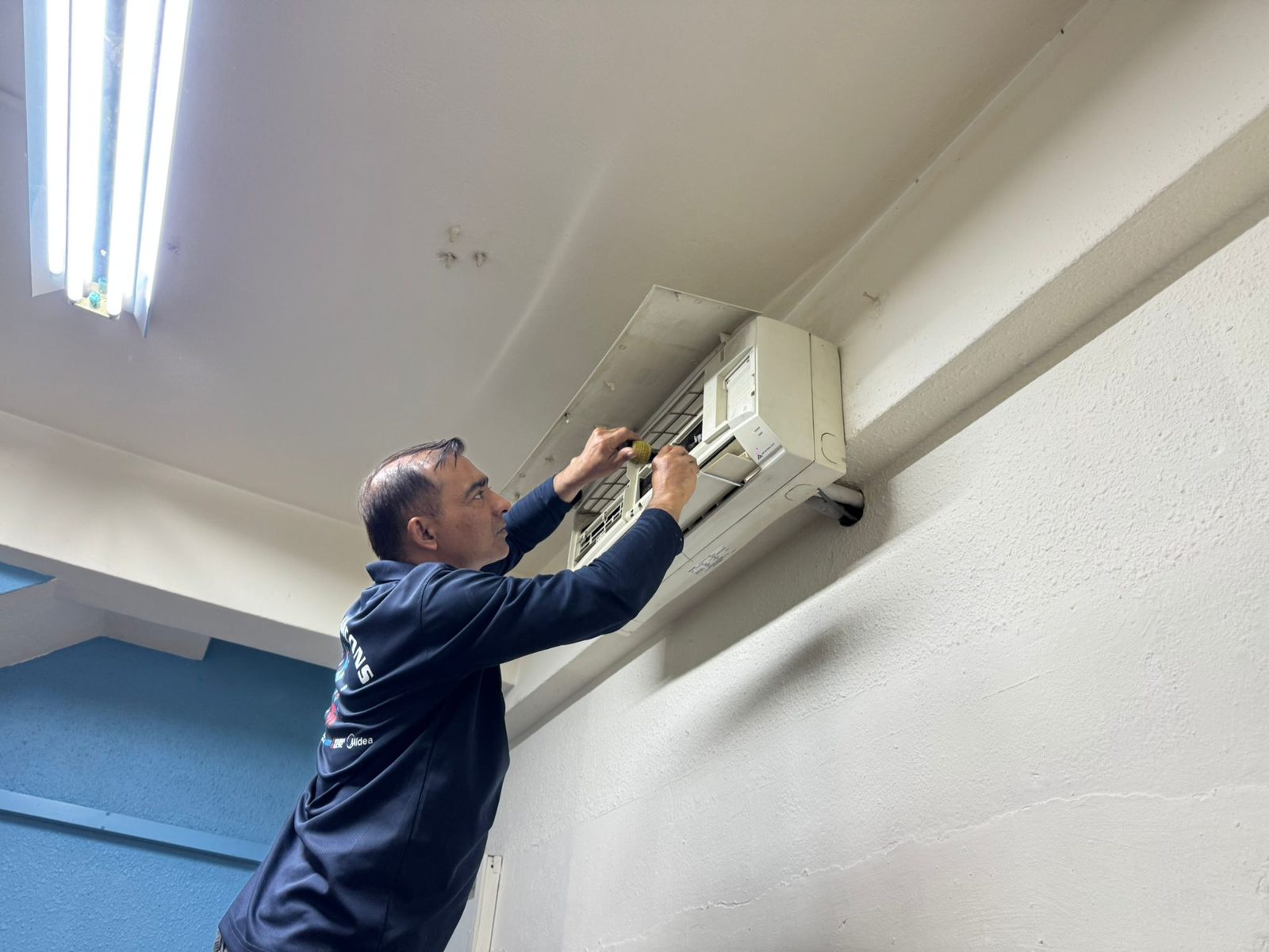 A Senpai technician in company polo servicing a wall-mounted aircon unit
